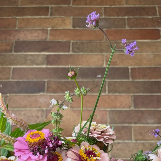 A loose bouquet of pink zinnias, dahlias, and airy purple stems against the porch brick