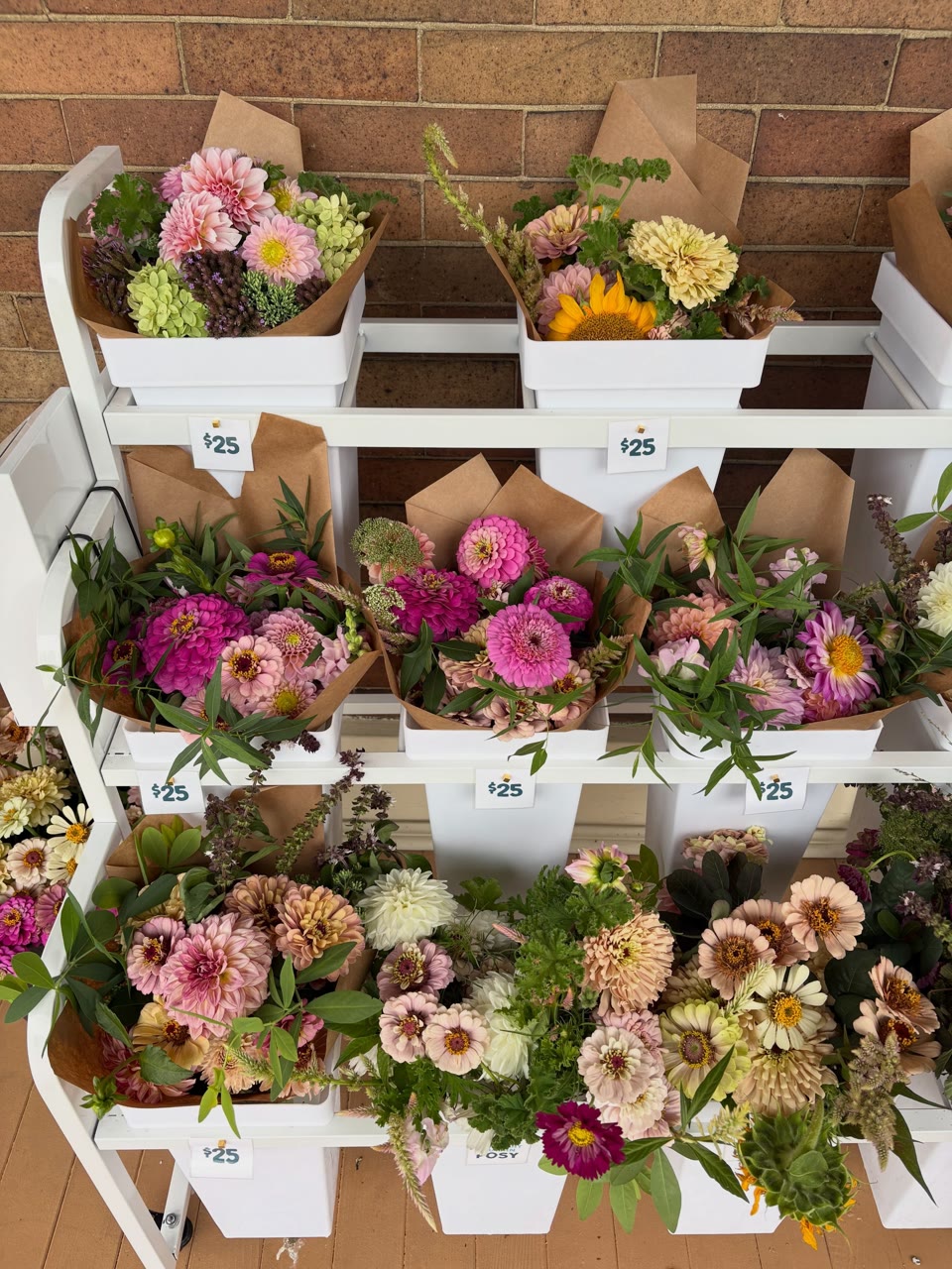 Rows of wrapped pink, yellow, and white bouquets displayed against the porch brick